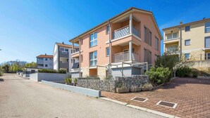 A multi-story residential building with balconies, a stone retaining wall, and a paved driveway. - Holiday apartment with balcony and air conditioning (Čižići)