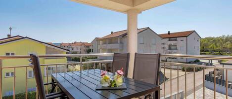 A balcony with a table and chairs, two drinks on the table, and a view of neighboring buildings.