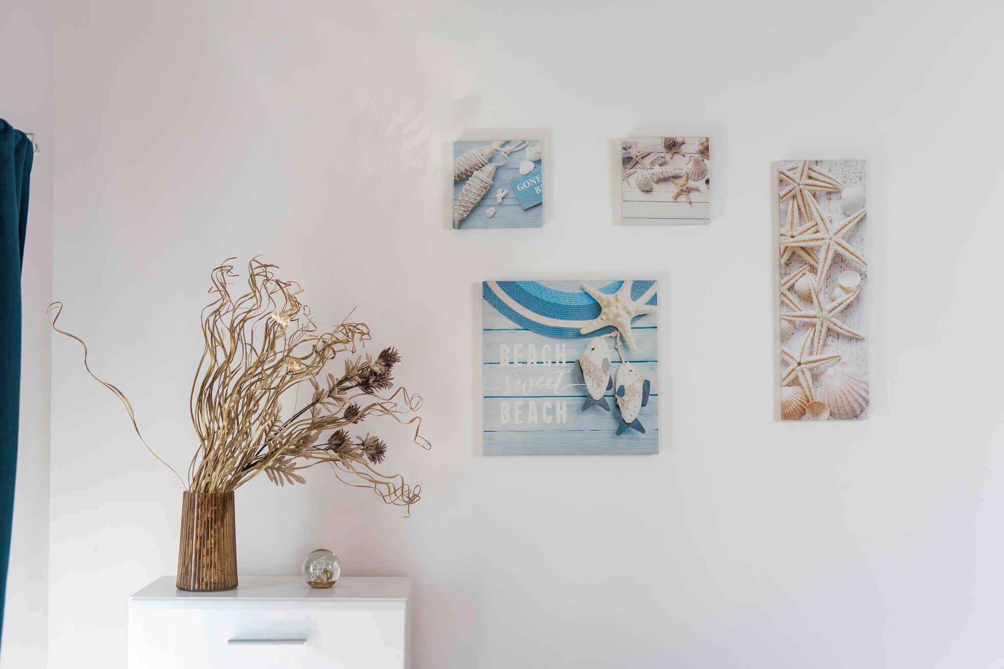 A wall with four framed artworks depicting beach scenes and sea life.