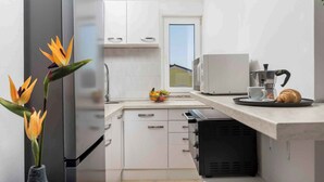 A modern kitchen with white cabinets, a built-in oven, a coffee maker, and a fruit bowl on the counter. - Holiday apartment with balcony and air conditioning (Čižići)