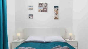 A hotel room with a bed, two nightstands, a teal bedspread, two rolled towels, and four framed pictures on the wall. - Holiday apartment with balcony and air conditioning (Čižići)