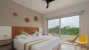 A bedroom with a large bed, a wooden headboard, a balcony with a yellow chair, and a view of greenery. - Private condo ideal for group/family, 12 people (Tulum)