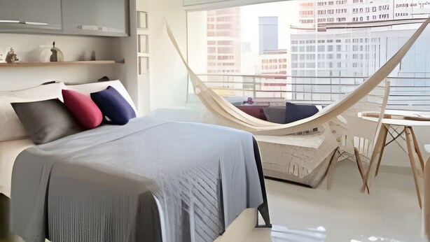 A modern bedroom with a bed, pillows, a hammock, and a city view. - Condomínio ver de Panorama (Sao Paulo)