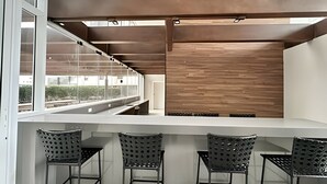 A modern bar area with a white countertop and metal chairs. - Condomínio ver de Panorama (Sao Paulo)