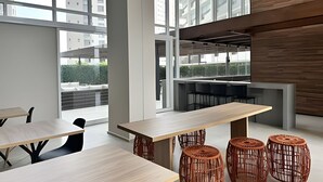 A modern office space with large windows, wooden tables, and wicker stools. - Condomínio ver de Panorama (Sao Paulo)