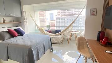 Quarto moderno com cama, rede, mesa pequena e vista para a cidade.