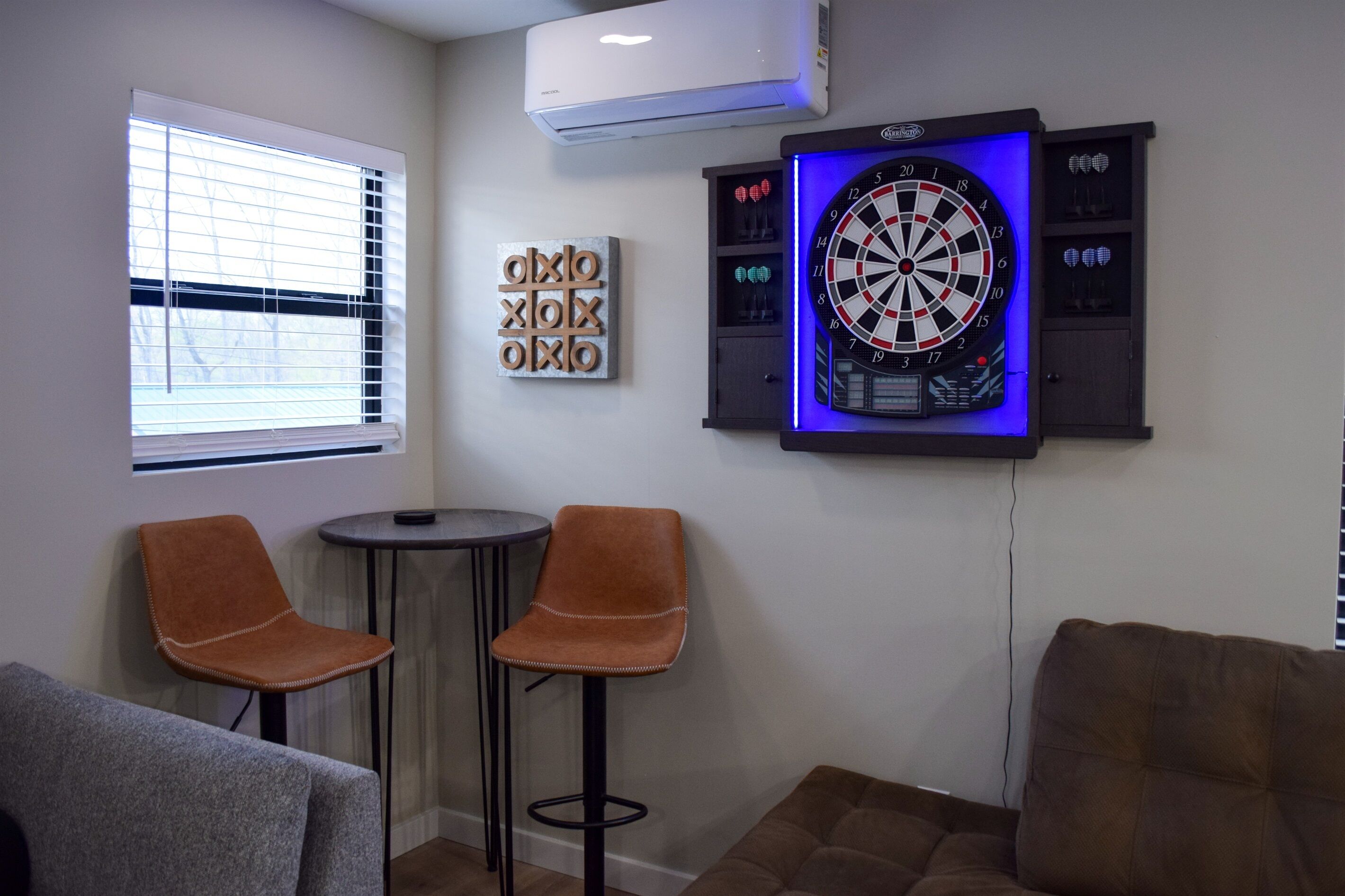 A room with a dartboard, two chairs, a small table, and a couch.