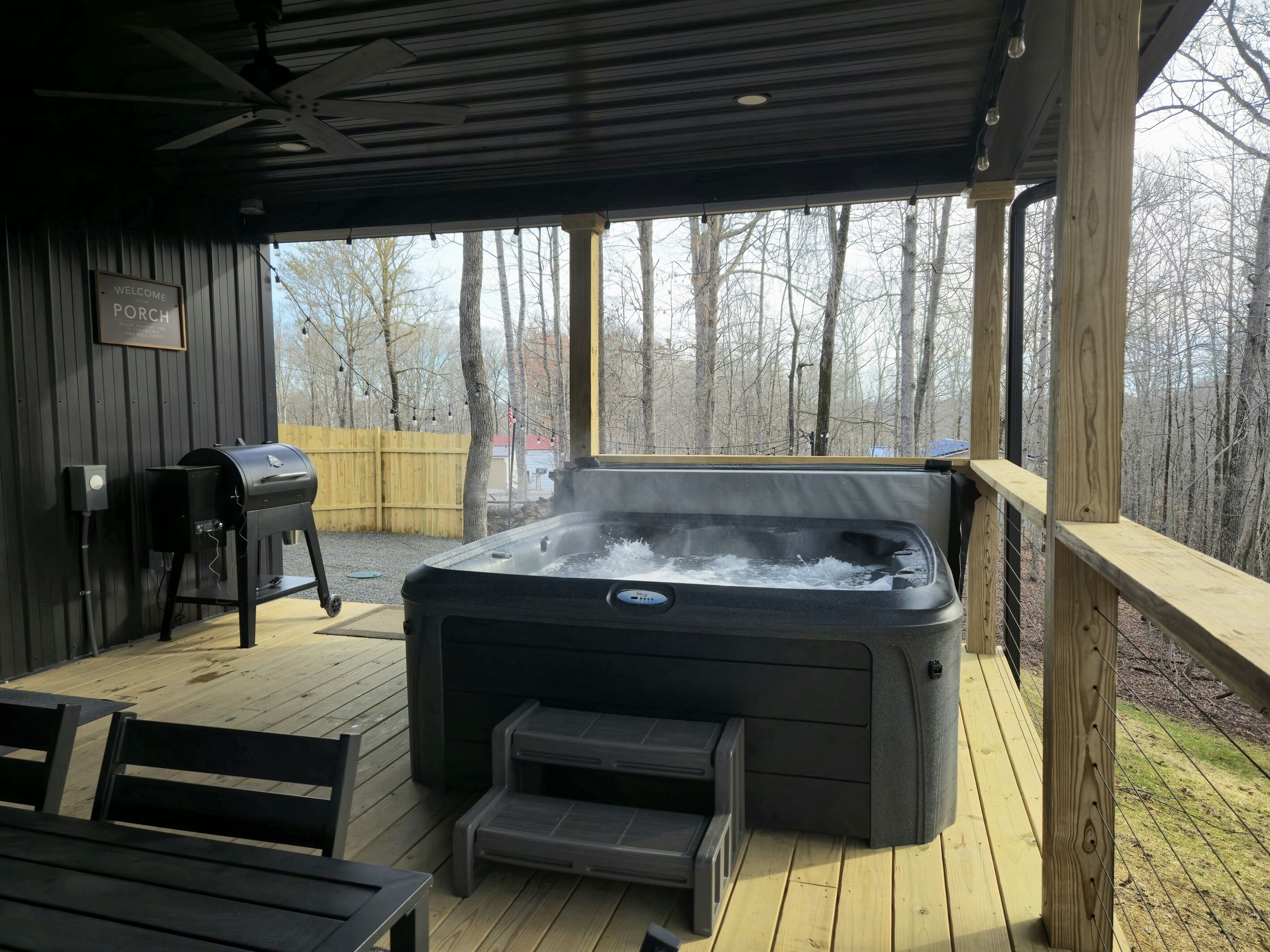 A hot tub on a wooden deck with a grill and a welcome sign.
