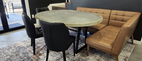 Una sala de estar moderna con una mesa redonda, dos sillas negras, un sofá de cuero marrón y una escalera frente a una pared oscura.