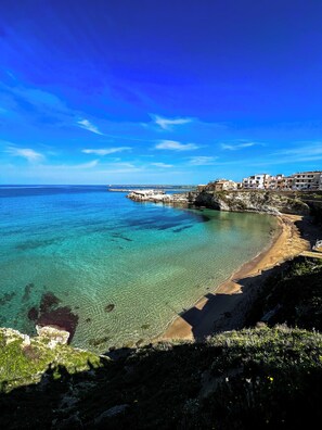 Vista costera con aguas turquesas cristalinas, una playa de arena y edificios a lo largo de la orilla.