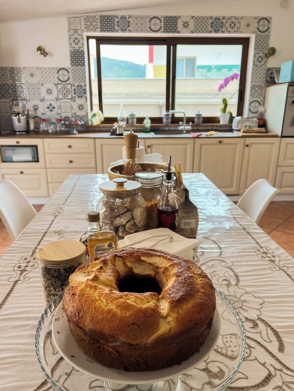 Una cocina con un ventanal grande, una mesa con un pastel y diversos utensilios de cocina.