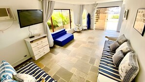 A spacious living area with a flat-screen TV, a blue sofa, a striped sofa, and a staircase leading to an outdoor area. - Cobertura Triplex no Guarujá SP 1 (Guaruja)