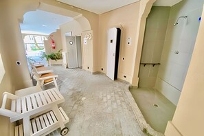 Un couloir donnant sur un espace de détente, comprenant une douche, un coin salon avec des bancs et une petite table.