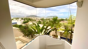 A balcony with a view of a coastal town, including buildings and palm trees. - Cobertura Triplex no Guarujá SP 1 (Guaruja)