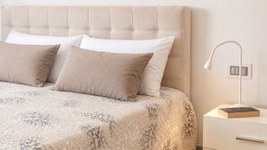 A bed with a tufted headboard, two pillows, a patterned bedspread, a bedside table with a lamp, and a book. - Suite LE Vele 1 in Gallipoli (Gallipoli)
