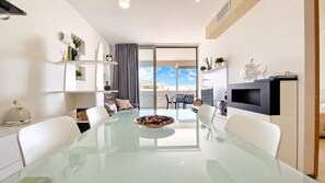 Ein modernes Wohnzimmer mit einem Glastisch, weißen Sofas, einem Flachbildfernseher und einem Balkon mit Blick.