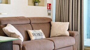 Ein braunes Sofa mit drei Kissen, einem Schild für Feuerlöscher und einem Fenster mit Vorhängen.