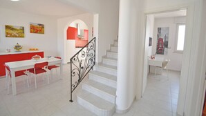 Un interior moderno con una escalera, un área de comedor con sillas rojas y una cocina con detalles en rojo.
