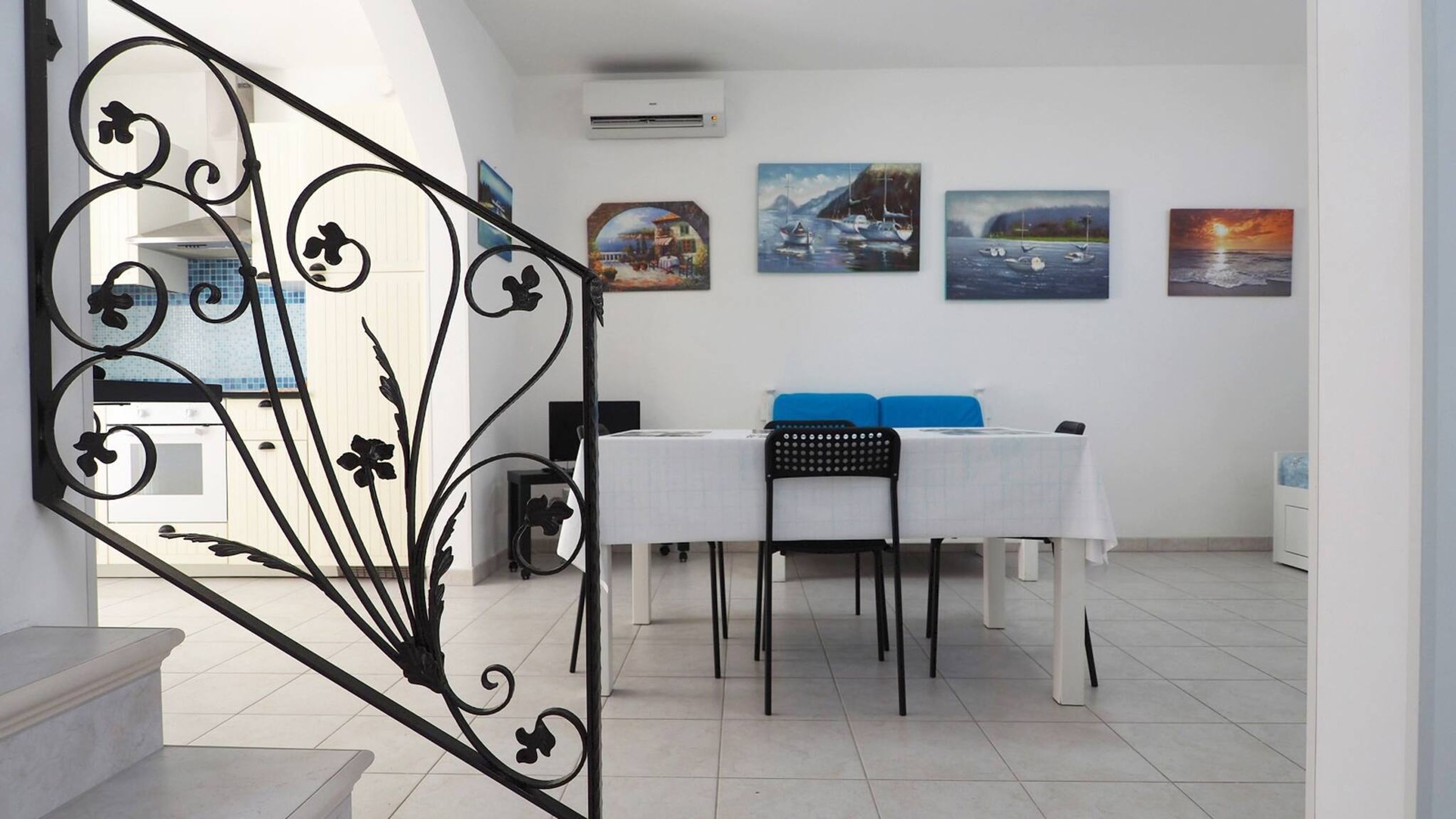 Un coin repas avec une table et des chaises blanches, une chaise noire avec un dossier, et un escalier avec une rampe noire.