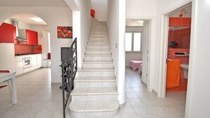Una escalera que conduce a un segundo piso, una cocina con armarios rojos y un baño con baldosas naranjas.