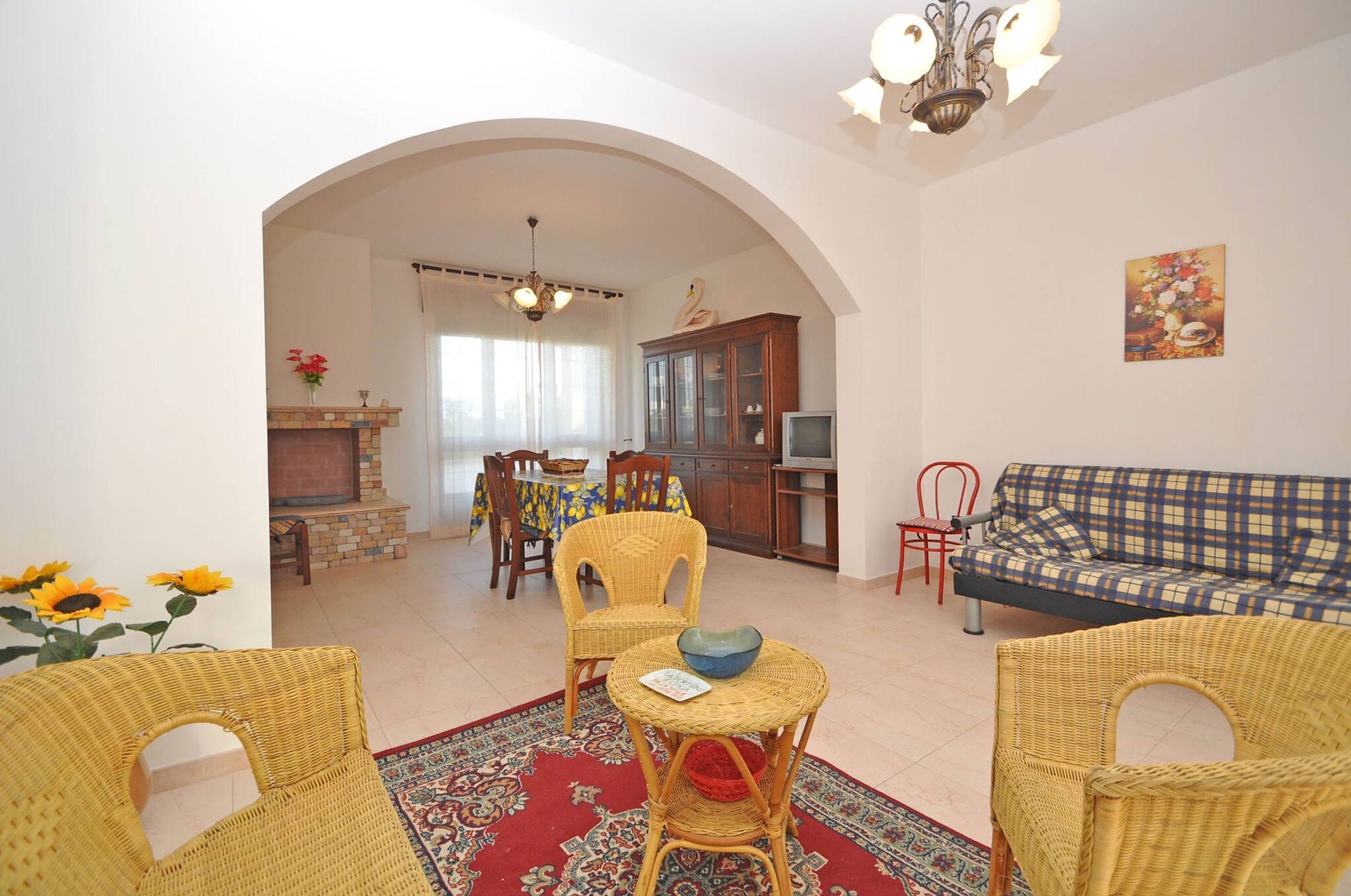 A living room with wicker furniture, a fireplace, a dining area with a table and chairs, and a sofa.