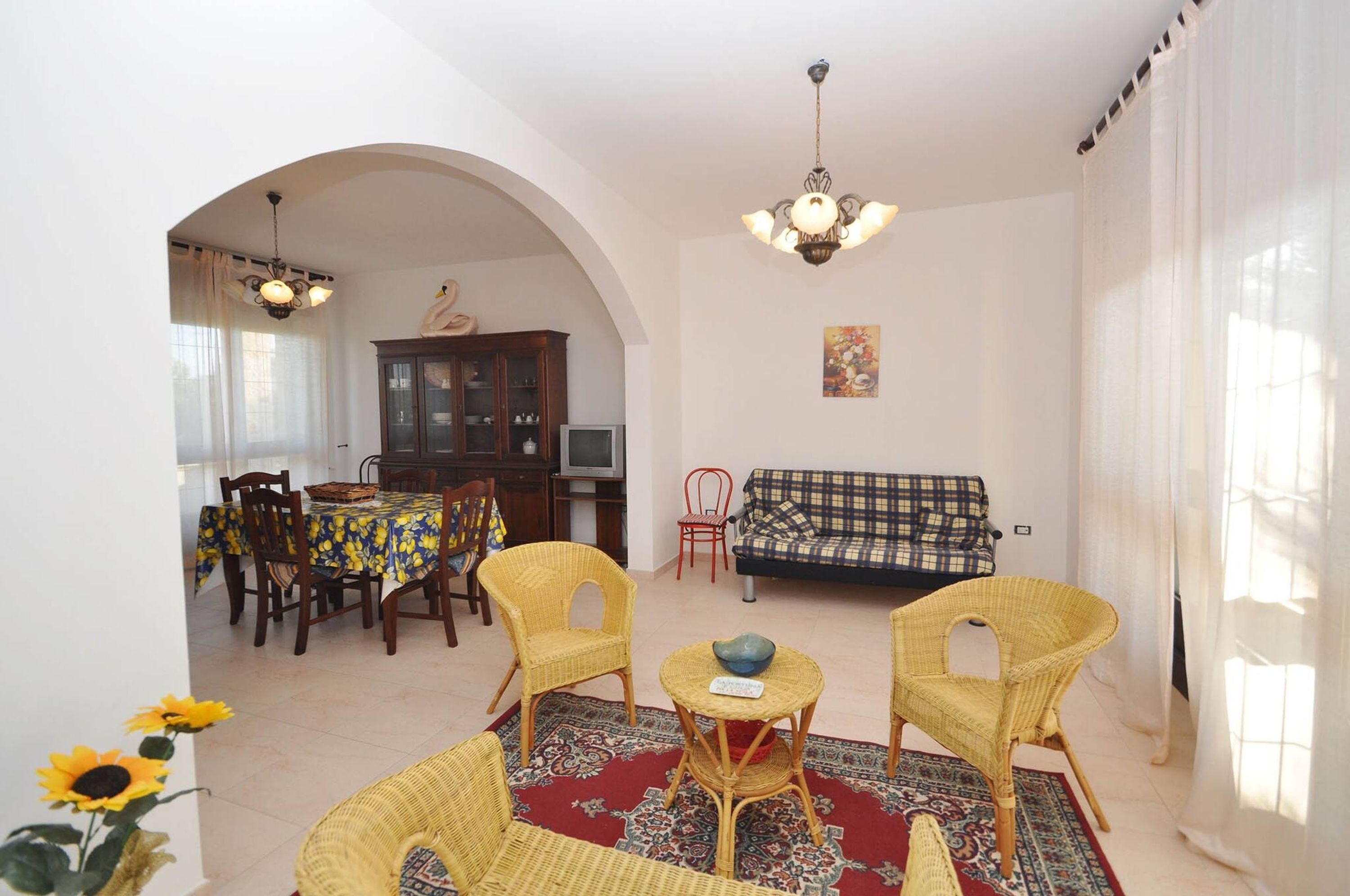 A living room with a dining area, a sofa, wicker chairs, a chandelier, and a television.