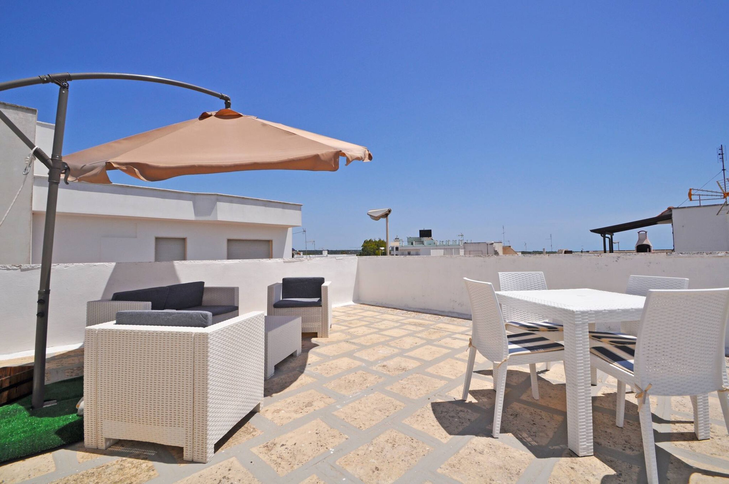 Terraza en la azotea con mobiliario de mimbre blanco, una mesa y un gran paraguas color beige.