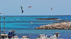 Un port de plaisance situé sur la côte, avec des bateaux, une digue rocheuse et des activités de kitesurf.