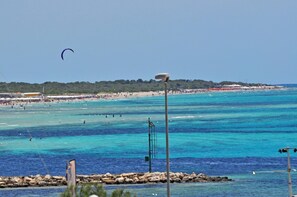 Une plage à l’eau turquoise et limpide, un parachute ascensionnel dans le ciel et une côte rocheuse.