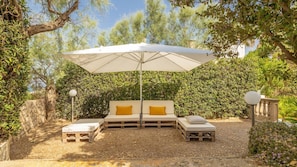 Un espace de détente extérieur accueillant, avec un parasol blanc, des bancs en bois et un banc rembourré agrémenté de coussins jaunes.