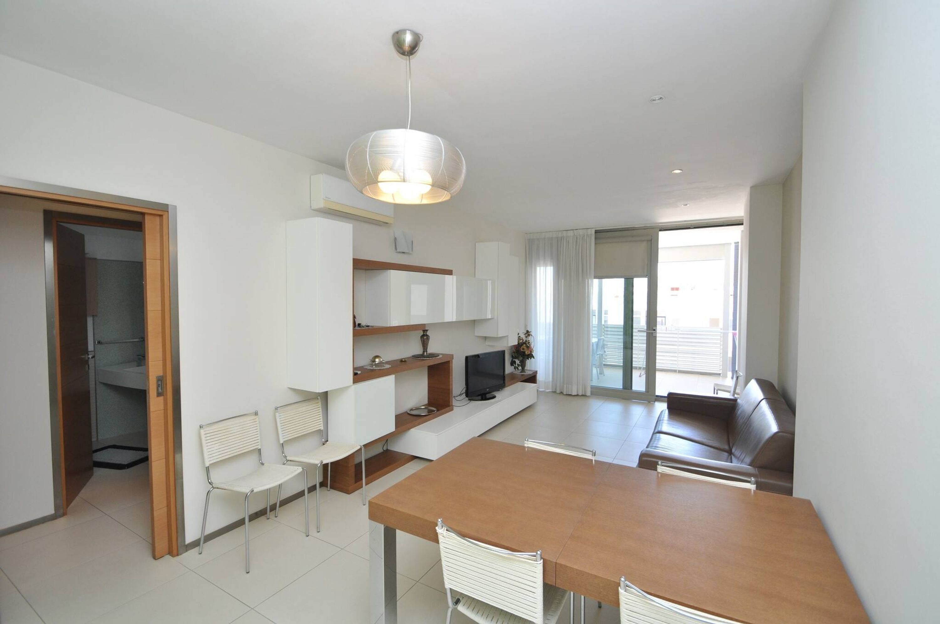A modern kitchen with white cabinets, a wooden dining table, and a built-in TV.