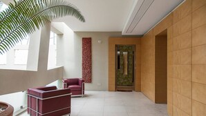 Um lobby moderno com teto alto, uma grande planta em vaso e uma área de estar com sofás vermelhos.