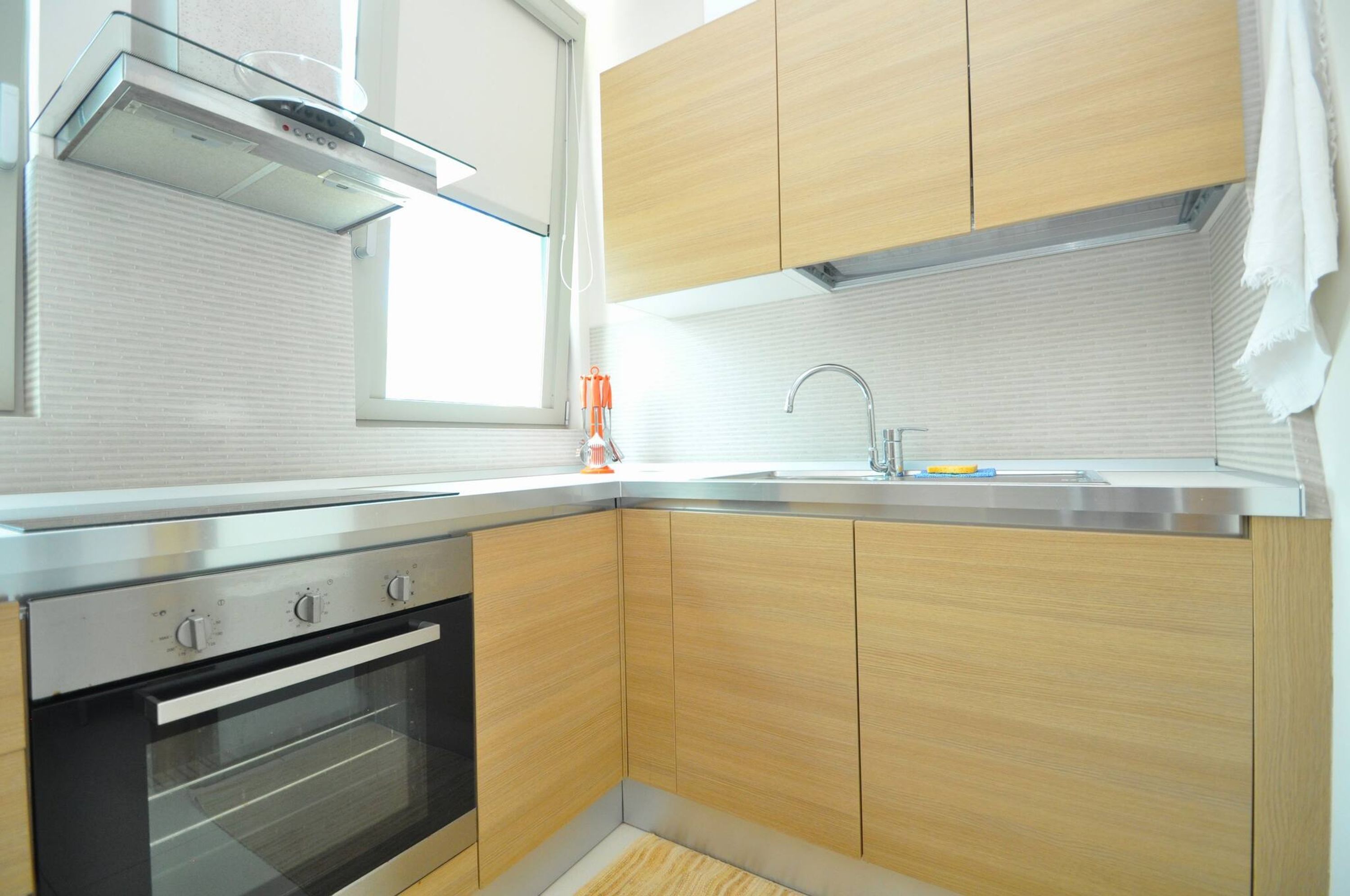 A modern kitchen with wooden cabinets, a stainless steel oven, a window, and a sink.