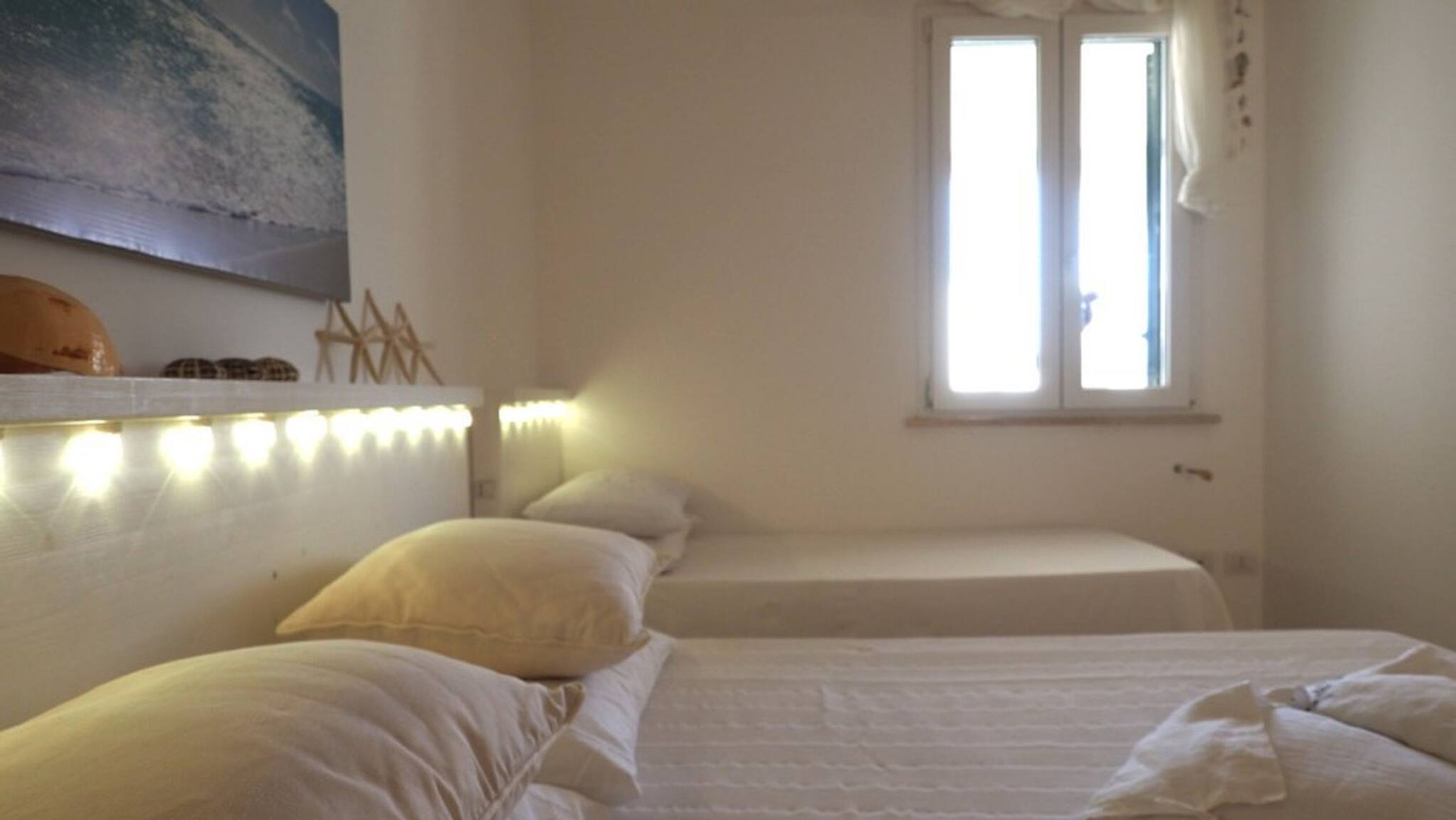 A bedroom with two beds, a window, and a wall-mounted light fixture.