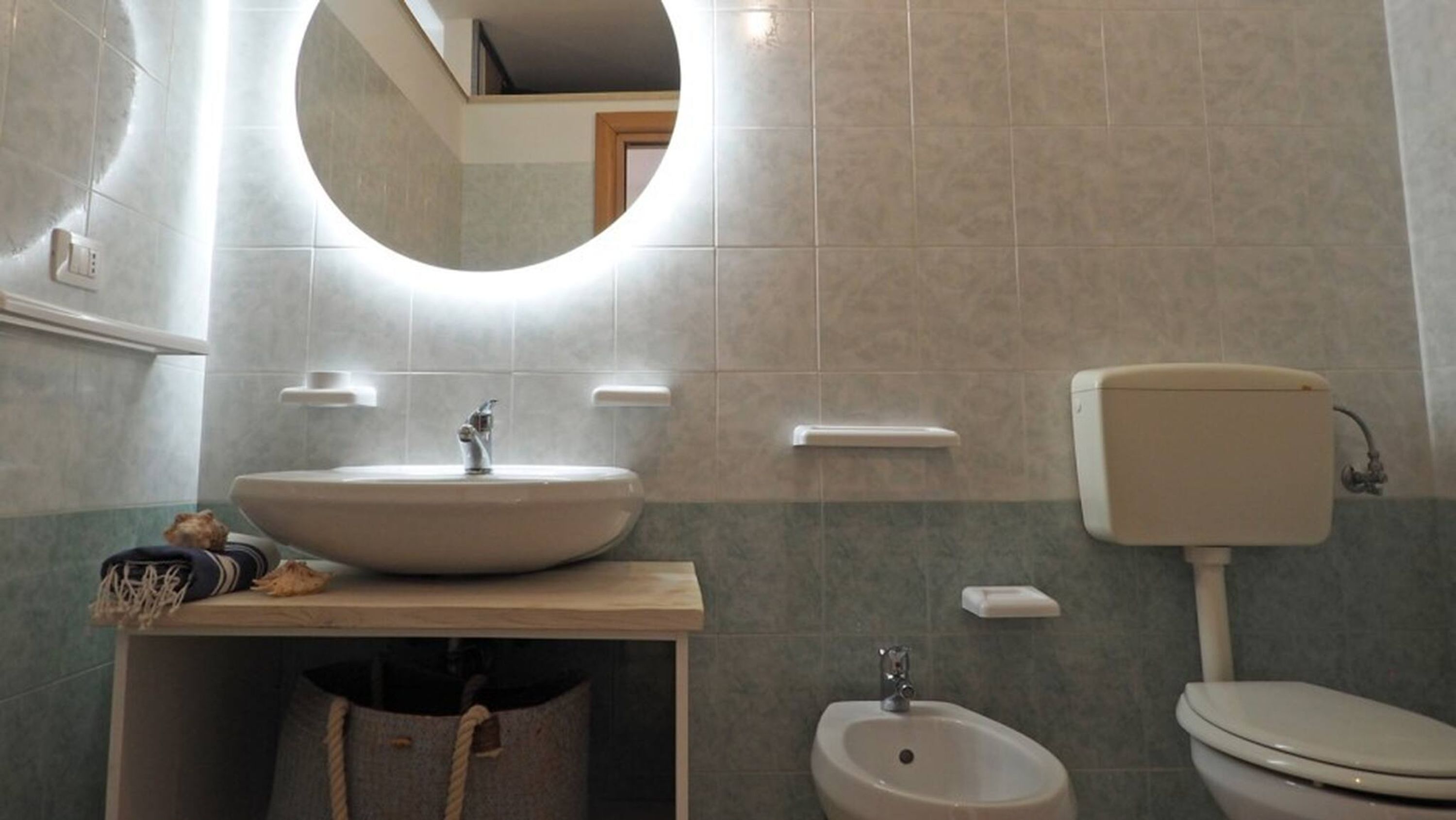 Een badkamer met een ronde spiegel, een wastafel, een bidet en een toilet.