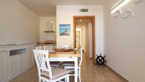A dining area with a wooden table and white chairs, a painting on the wall, and a ship's wheel decoration. - Villa DEL Mare 2 in Torre San Giovanni (Ugento)