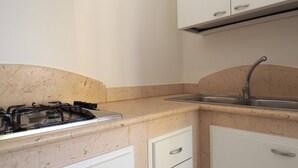 A kitchen with a gas stove, a sink, and white cabinets. - Villa DEL Mare 2 in Torre San Giovanni (Ugento)