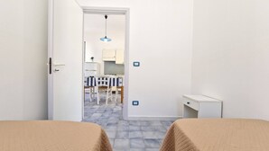Une chambre avec deux lits, une petite table de chevet et une porte donnant sur un coin cuisine.