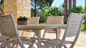 A set of four white wicker chairs and a table with a small potted plant on it, placed outdoors with a stone pillar and greenery in the background. - Villa Paradiso in Marina di Mancaversa (Taviano)