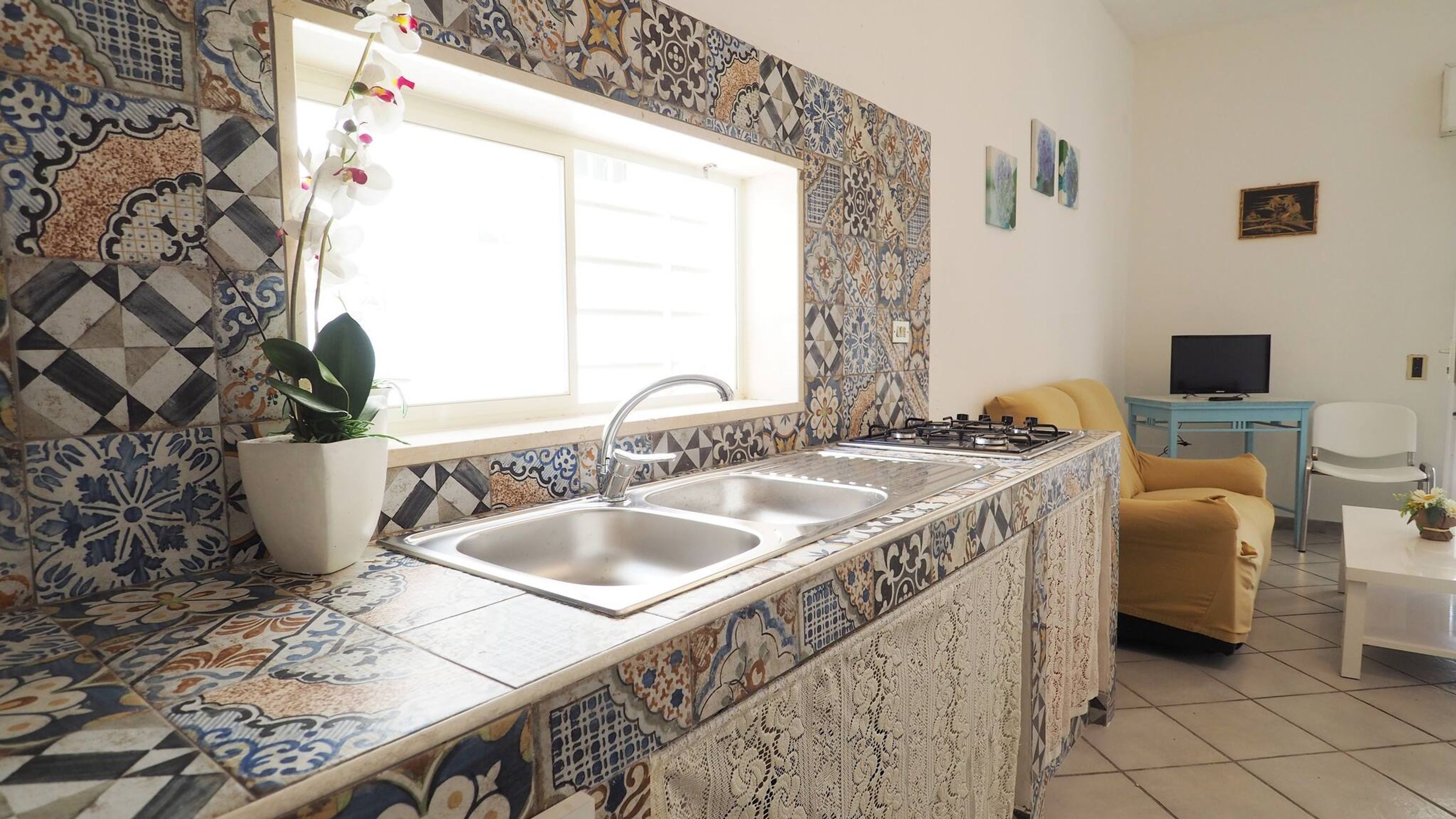 A kitchen with a sink, stove, and a window. There is a plant on the counter and a chair in the background.