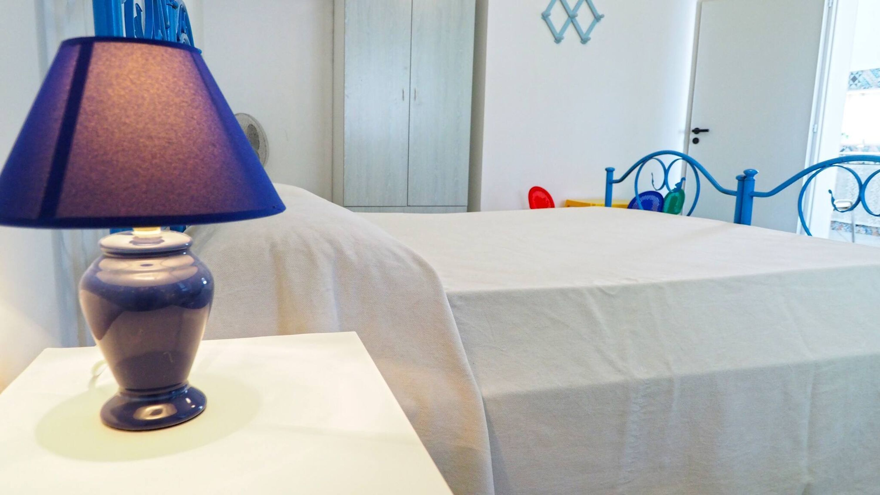 A room with a bed covered in white sheets, a blue lamp on a bedside table, and a blue metal bed frame.