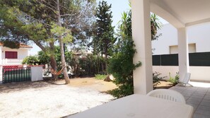 A covered outdoor area with a white table and chairs, surrounded by trees and a fenced garden. - Villa Akire 8 Posti 3 Camere 100 mt dal Mare (Racale)