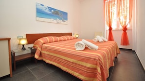 A hotel room with a bed, a nightstand, a lamp, a painting of a beach scene, and a window with orange curtains. - Residence Arainn Kalepolis - Pool Sleeps 5 Wifi (Ugento)
