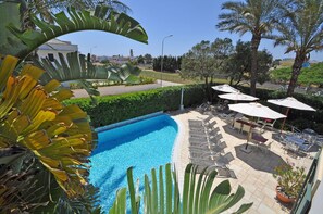 Una piscina con sillas de descanso y sombrillas, rodeada de plantas tropicales y vistas al paisaje.