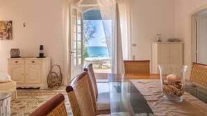Un coin repas avec des chaises en osier, une table en verre et une vue sur l’océan par une porte.