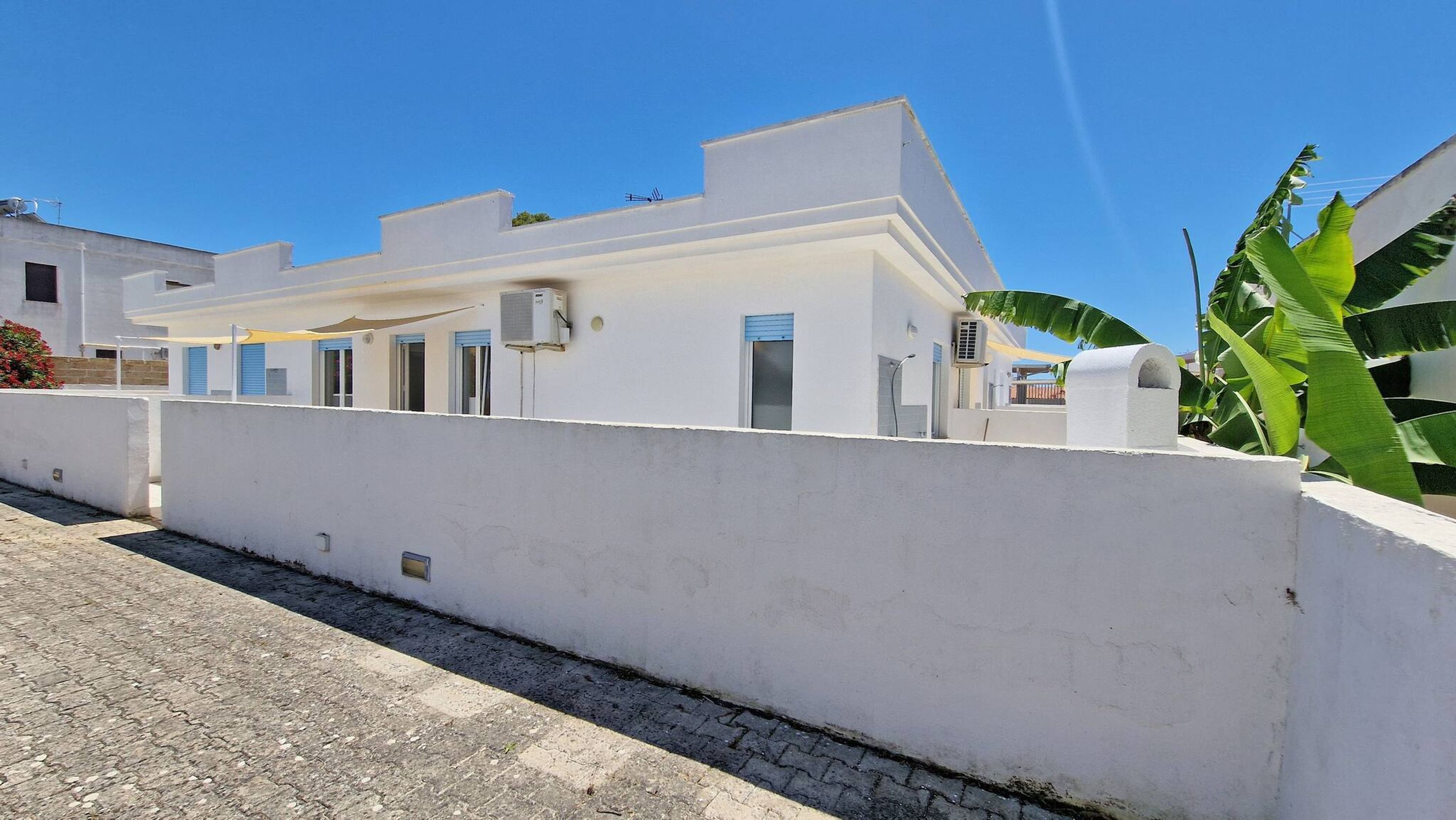 A white building with a flat roof, a covered outdoor area, and a paved street.