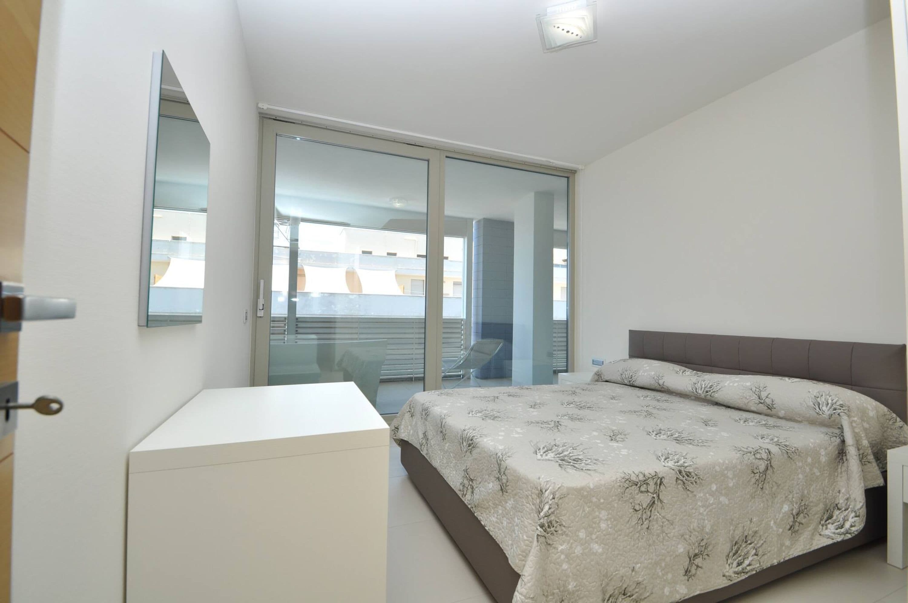 Un dormitorio con cama, escritorio y puerta corrediza de vidrio que da a un balcón.