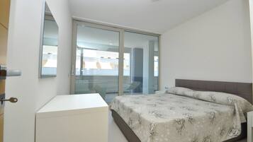 Un dormitorio con cama, escritorio y puerta corrediza de vidrio que da a un balcón.