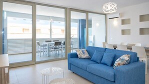 A modern living room with a blue sofa, two patterned cushions, a small round table, and a hanging light fixture. - Appartamento LE 5 Vele (Gallipoli)