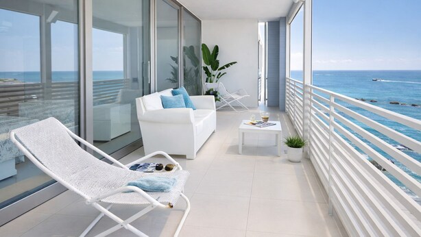 A balcony with a white sofa, a white lounge chair, a small table with a plant, and a view of the ocean. - Appartamento LE 5 Vele (Gallipoli)